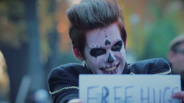 Funny guy with zombie makeup on face standing in street with free hugs sign 