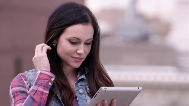 Up close veiw of woman running fingers through hair while looking at tablet.