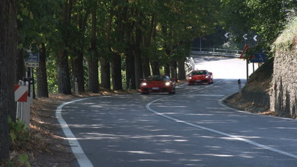 2 Ferrari cars driving on a country road in Italy.