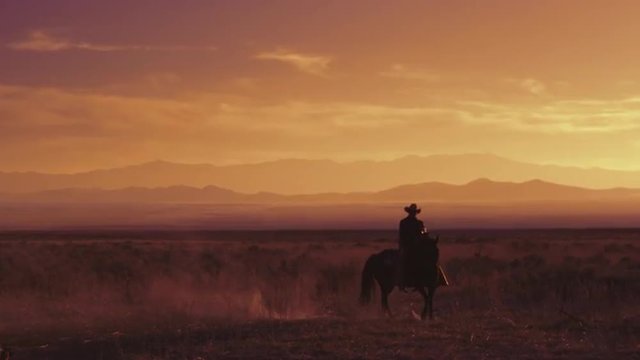  Lone western cowboy riding a horse at sunrise sunset, slow motion