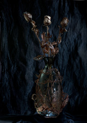 Still - metal roses in a glass bottle on a dark textural background