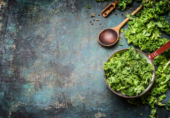 Fresh kale in cooking pot with wooden spoon on  rustic background, top view, border. Healthy food...