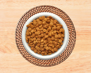 Dry cat food in plate on wicker placemat on wooden background