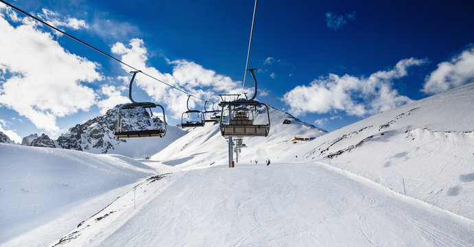 Winter mountains panorama with ski slopes and ski lifts. Skiers going down the slope under ski lift.