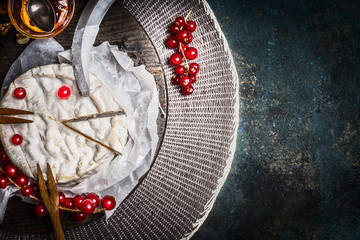 Camembert cheese plate with red currant berries and sauce on rustic background, top view, place for text. Traditional milk dairy product