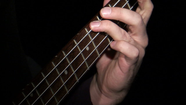 Neck of a bass guitar being played against a black background.