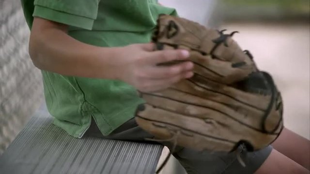 Slow motion of boy holding baseball mitt then setting it down next to him on bench.