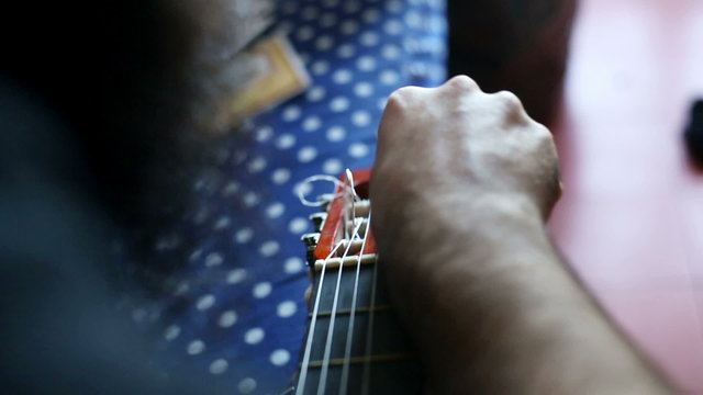 man changing strings on a classical guitar, indoor at home, natural light.