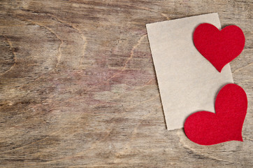 Two Red fabric hearts with sheet of paper lying on old wooden ba