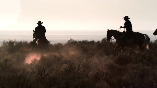 Cowboys galloping through the dusty desert in slow motion with lens flare..