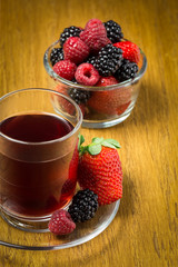 Fruit tea in glass cup and glass bowl with strawberries, raspberries and blackberries