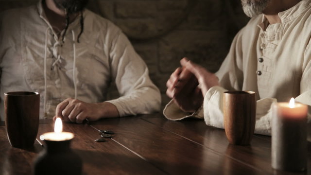 two medieval looking men are gambling with dices, one is winning and gets the whole stake of gold nuggets