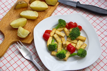 pieces of tofu served with broccoli, tomatoes and baked potatoes