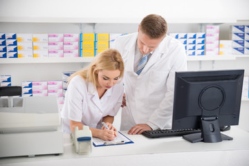 Fototapeta na wymiar Pharmacists Maintaining Checklist At Counter In Pharmacy