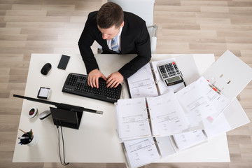 Businessman Analyzing Documents At Computer Desk