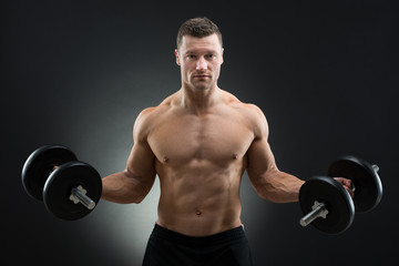 Fototapeta na wymiar Confident Muscular Man Holding Dumbbells