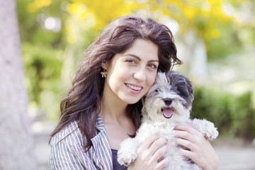 smiling young woman hugging with her small white poodle dog outdoor