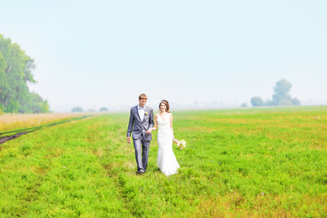 happy beautiful bride and groom walking on field