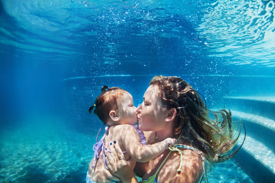 Happy family - mother kiss baby girl dive down with fun in beach pool. Healthy lifestyle, active parents, people water sport activity and underwater swimming lessons on summer vacation with child.