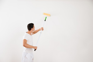 Man Using Paint Roller On White Wall