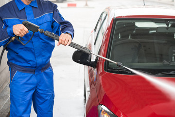 Worker Cleaning Car With Jet Sprayer At Service Station