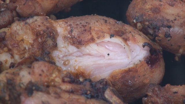 Checking undercooked chicken drumstick being scorched on the fire pit's grill. This is close up footage of marinated with salt and dry garlic chicken drumstick with skin.