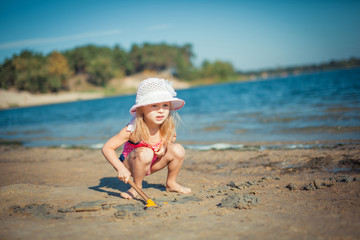 Fototapeta na wymiar Adorable toddler girl playing with beach toys on white sand beach.