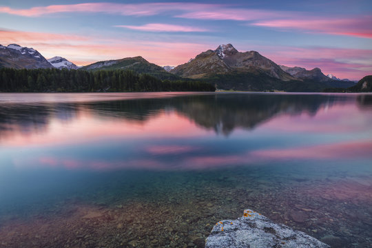Pink sky at dawn illuminates the peaks reflected in Lake Sils, Engadine, Canton of Graubunden