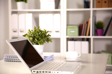 Close up view of a work desk interior with a laptop computer, a cup of coffee and white curtains on a sunny day