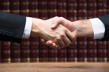 Judge And Client Shaking Hands Against Books - obrazy, fototapety, plakaty