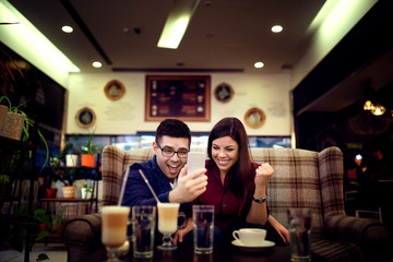 Lovely young couple looking at smart phone at cafe in trade center. Copy space for your text. Shallow depth of field. Very useful photo for processing with one click on edit image.
