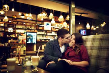 Lovely young couple at cafe bar. He is kissing her.