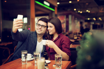 Happy young couple taking selfie with smart phone at cafe in mall. Copy space for your text. Shallow depth of field. Very useful photo for processing with one click on edit image.