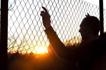 silhouette of a man behind the fence on the background of sunset