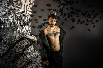 young trendy man with a beard, dressed in a fashionable jacket, at the bottom of a dungeon with brick walls and poor lighting. Paper black butterflies on the wall
