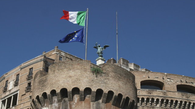 Two flags on a flag pole atop a stone structure in Rome Italy.