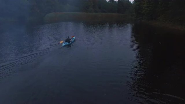 Aerial drone shot of a man in a blue kayak in a river in the forest.