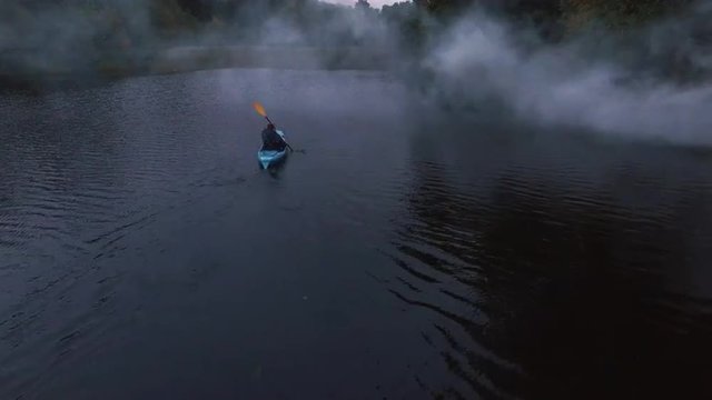 Aerial drone shot of a man in a blue kayak in a river in the forest.