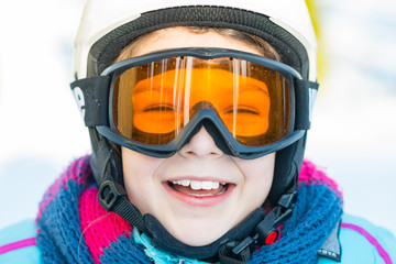 Ski, skier girl, winter vacation - happy child girl in goggles and protective helmet enjoining winter holidays