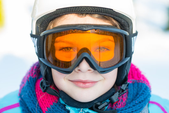 Ski, skier girl, winter vacation - happy child girl in goggles and protective helmet enjoining winter holidays