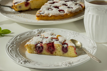Homemade Cherry Pie on a large white plate and a separate piece of it in a white plate on a white round coffee table, sunny light