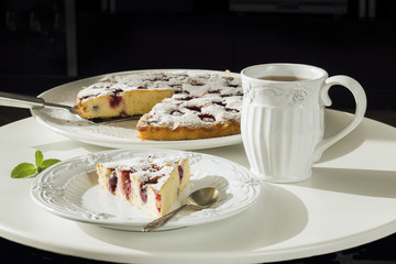Homemade Cherry Pie on a large white plate and a separate piece of it in a white plate on a white round coffee table, sunny light