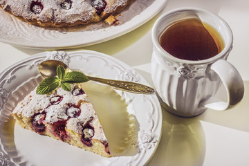 Homemade Cherry Pie on a large white plate and a separate piece of it in a white plate on a white round coffee table, sunny light