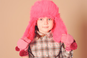 Young baby model in pink fur winter hat at beige background in studio