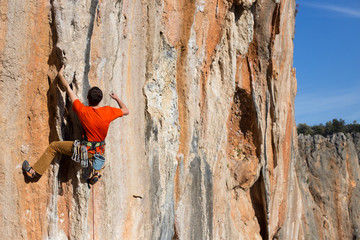 Young male climber hanging by a cliff.