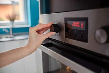 Woman regulates the temperature of the oven - obrazy, fototapety, plakaty