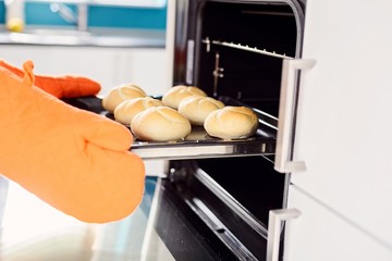 Close up of baker hands taking out hot rolls from the oven.