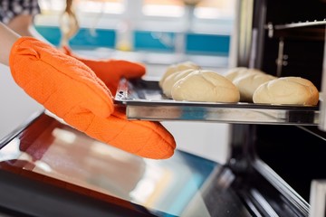 Close up of women hand taking out hot rolls from the oven.