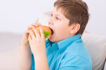 Chubby kid taking a bite off cheeseburger. 