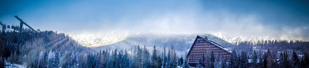 winter scenic panorama view of mountain with a hotel and ski jumping platform, sun covered with...